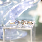 Two gold rings with gemstones on a clear stand with a blurred background